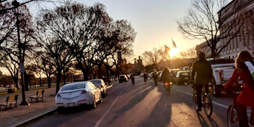 A staggered line of bicyclists glides down the tree-lined street beside the Capitol building in Olympia as the sun grazes the horizon